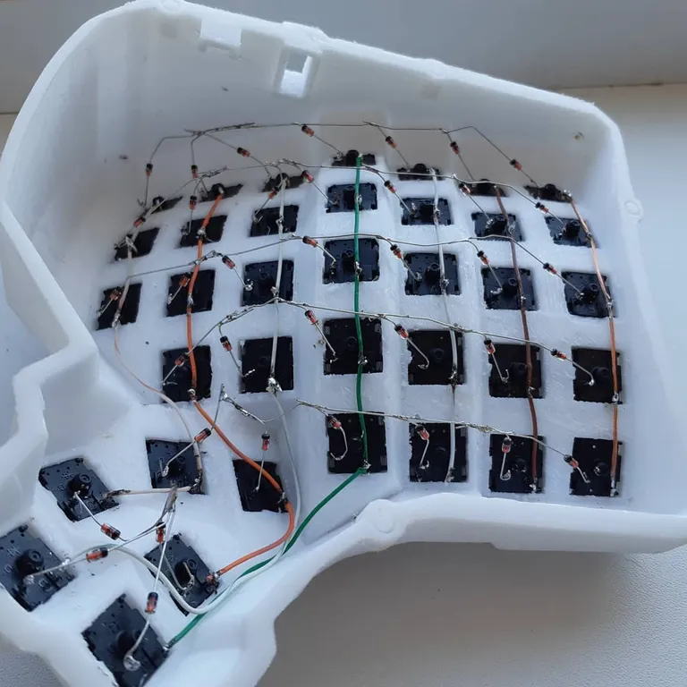 The finished hand-wired matrix inside the half: bent diode legs, orange and green wires, ugly but working