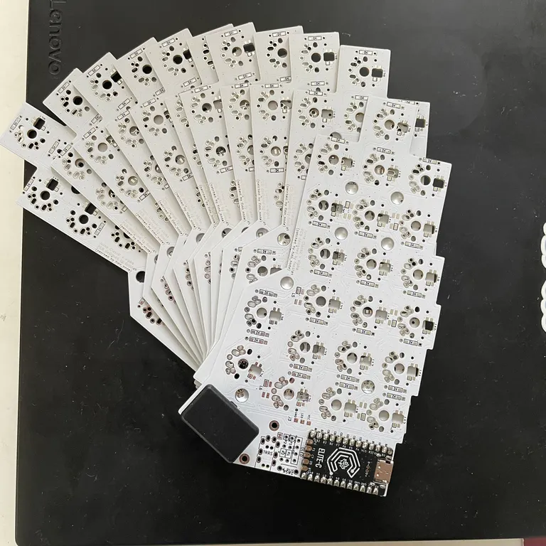 The whole JLCPCB batch fanned out on my laptop, a dozen white PCBs and an Elite-C controller